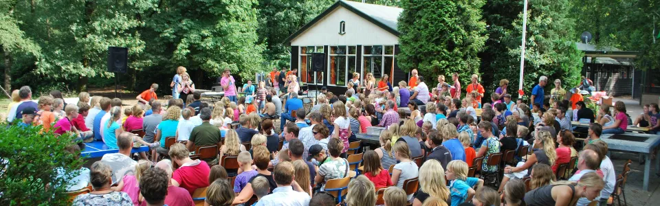 Volle picknicktafels met ouders en kinderen bij het kampgebouw
