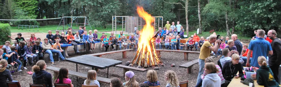 Deelnemers op houten banken rond een kampvuur