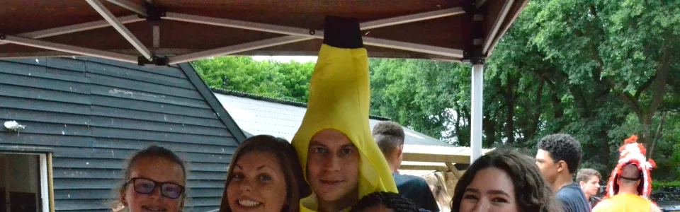 Deelnemers verkleed als banaan poseren bij het kampgebouw