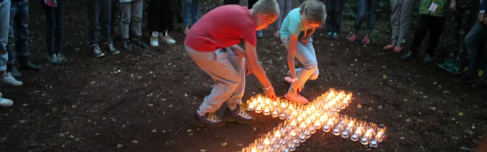 Kinderen leggen brandende kaarsjes in de vorm van een kruis op de grond