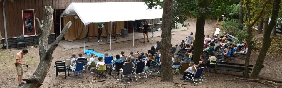 Deelnemers zitten onder de bomen bij het kampgebouw
