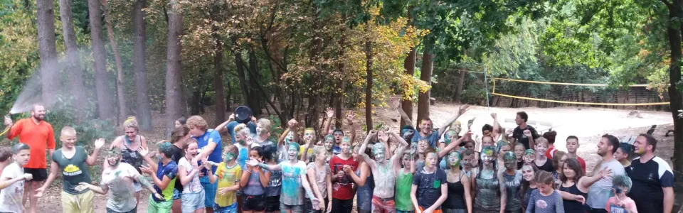 Grote groep deelnemers op het kampterrein tussen de bomen
