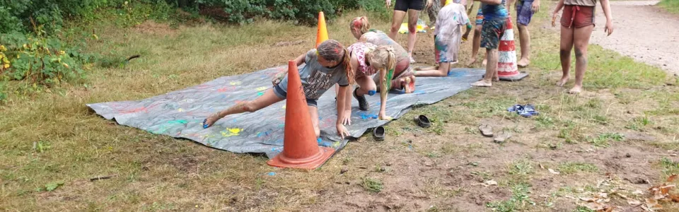 Deelnemers glijden over een nat zeil in het bos
