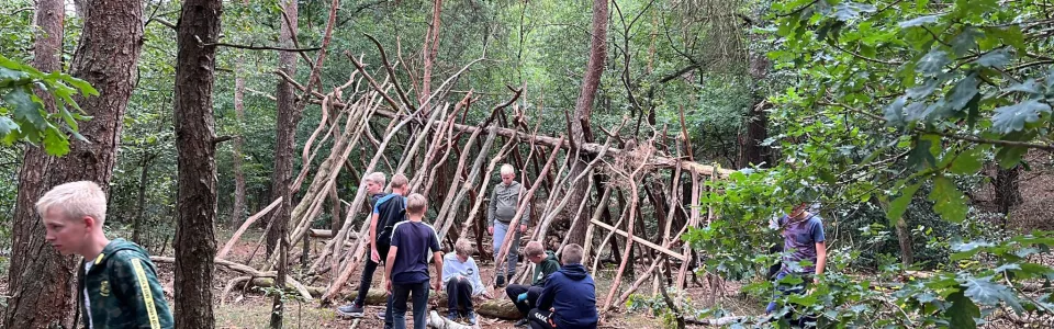 Deelnemers bouwen een hut van takken in het bos