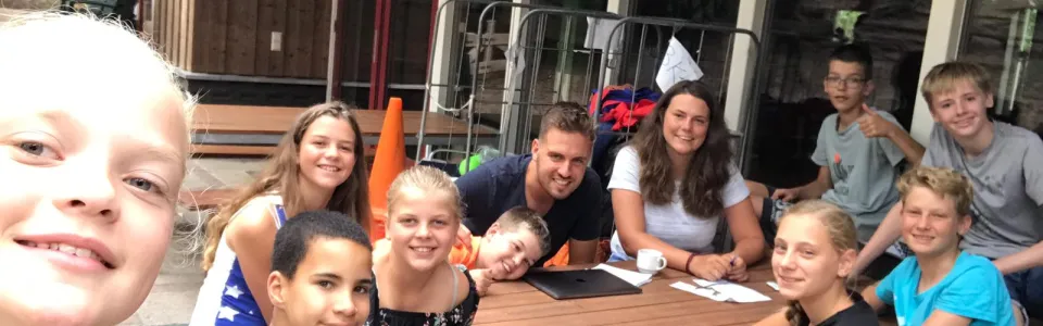Deelnemers met feestmutsen aan tafel bij het kampgebouw
