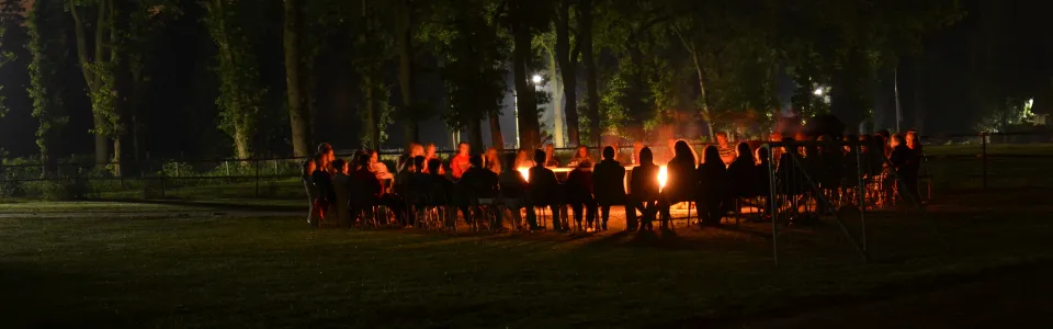 Groot kampvuur in het donker met deelnemers eromheen