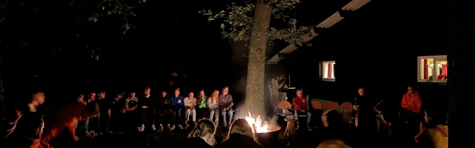 Deelnemers rond een kampvuur in het donker
