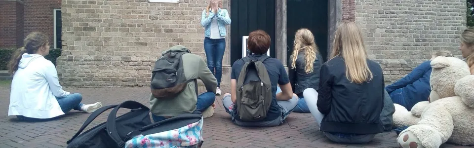 Deelnemers zitten met bagage tegen de muur van het gebouw