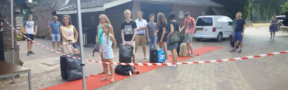 Deelnemers met bagage lopen over een rode loper