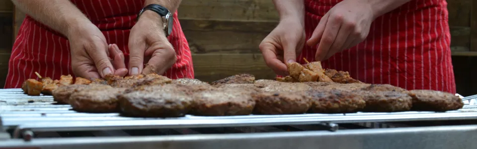 Handen leggen hamburgers op de barbecue