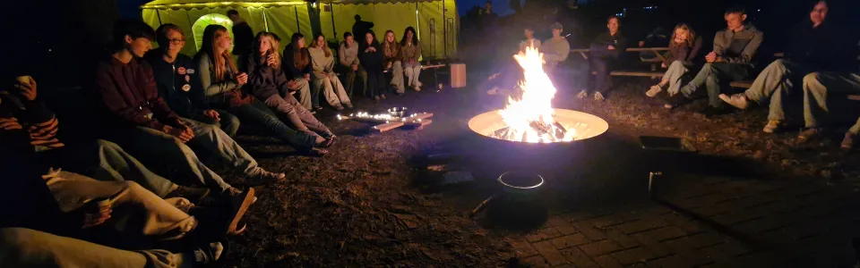 Tieners genieten samen rond het kampvuur tijdens de avondschemering