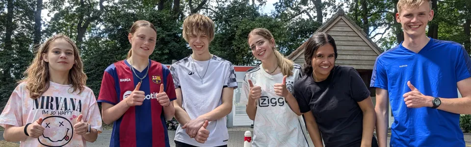Zes tieners steken samen lachend hun duimen op tijdens jeugdkamp