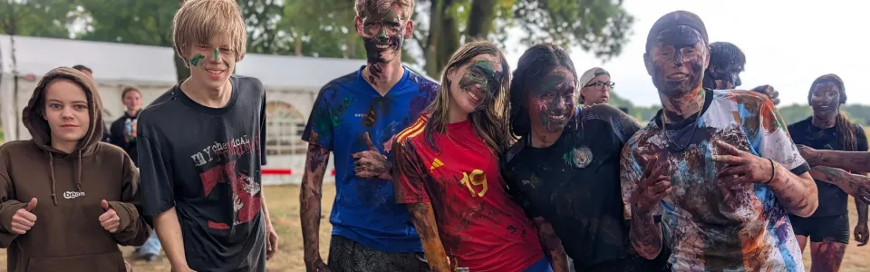 Tieners poseren lachend na een kleurrijk moddergevecht op kamp