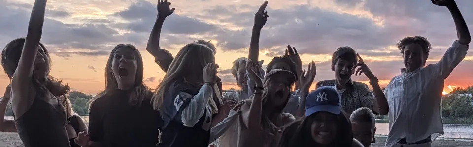 Juichende tieners springen samen op tijdens een kleurrijke zonsondergang