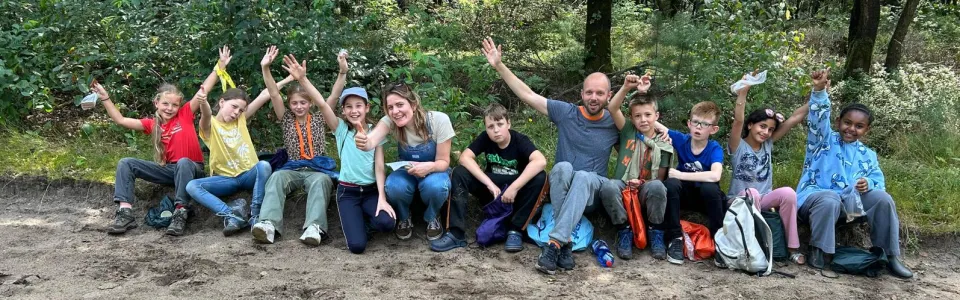 Kinderen en begeleiders zwaaien vrolijk tijdens een boswandeling