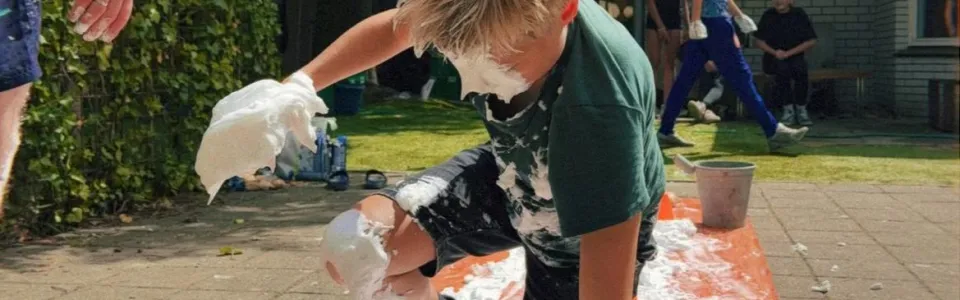 Tiener kruipt lachend door scheerschuim tijdens een zonnig kampspel