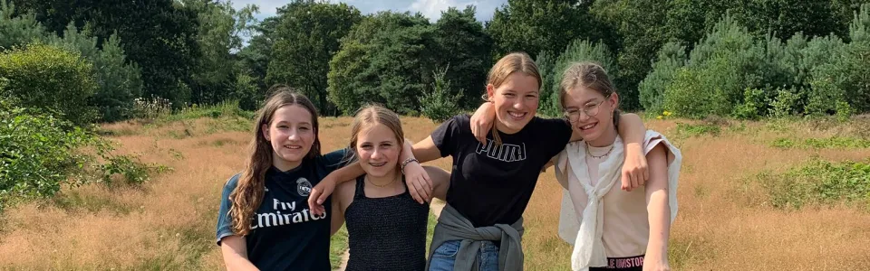 Vier tienermeiden lopen arm in arm over een zandpad