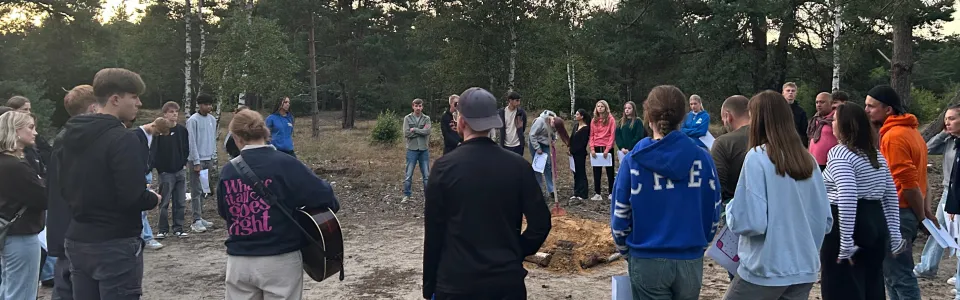 Tieners zingen samen in een kring tijdens een bosavond.
