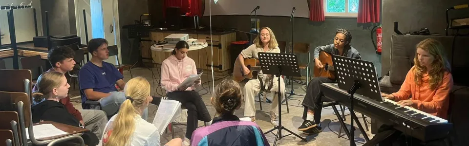 Tieners zingen samen met gitaren en piano in de kampzaal