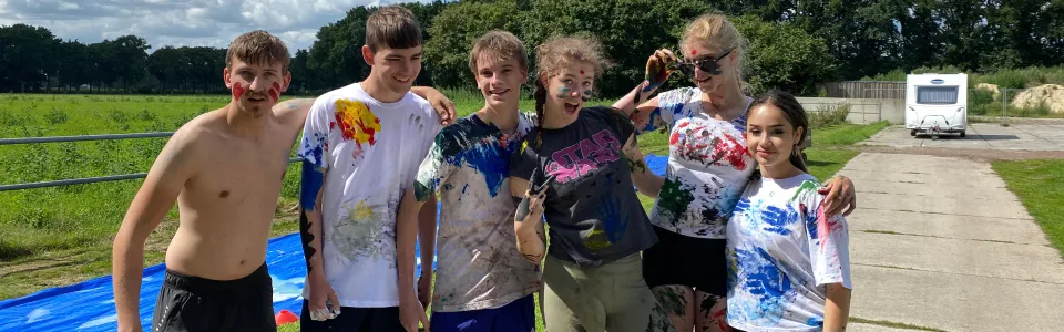 Tieners poseren lachend na een kleurrijk verfspel op kamp
