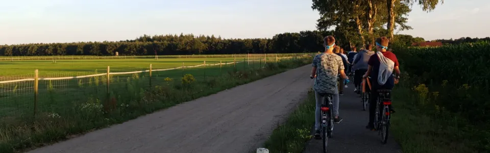 Deelnemers lopen en fietsen over een landweg bij zonsondergang