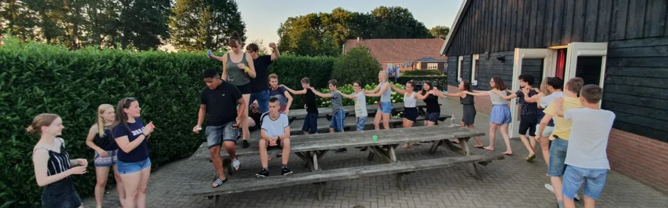 Deelnemers zitten op banken bij het kampgebouw