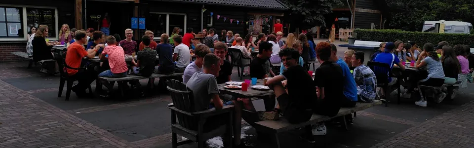 Deelnemers aan picknicktafels bij het kampgebouw