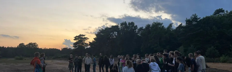 Deelnemers staan in een kring op de heide bij zonsondergang