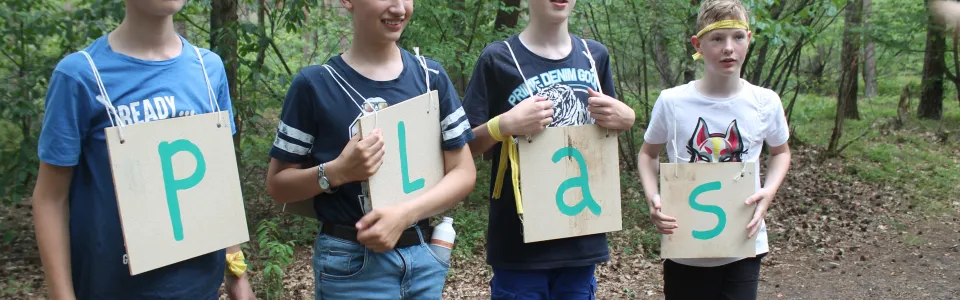 Deelnemers houden borden omhoog met de letters P L A S