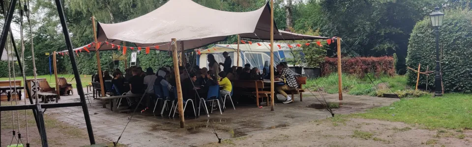 Deelnemers onder een partytent op een modderig terrein