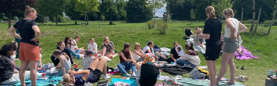 Deelnemers zitten op kleden in het gras