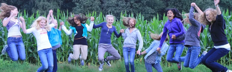 Groep jongeren springt tegelijk in de lucht in een weiland