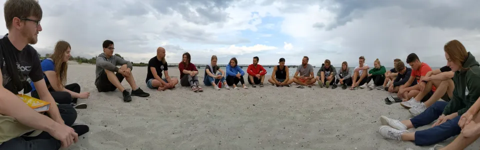 Deelnemers zitten op een rij in het zand