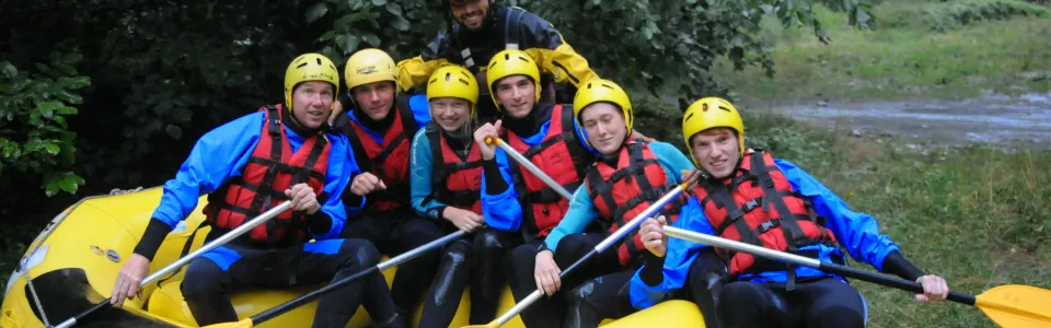 Deelnemers met helm en zwemvest in een raft op de rivier