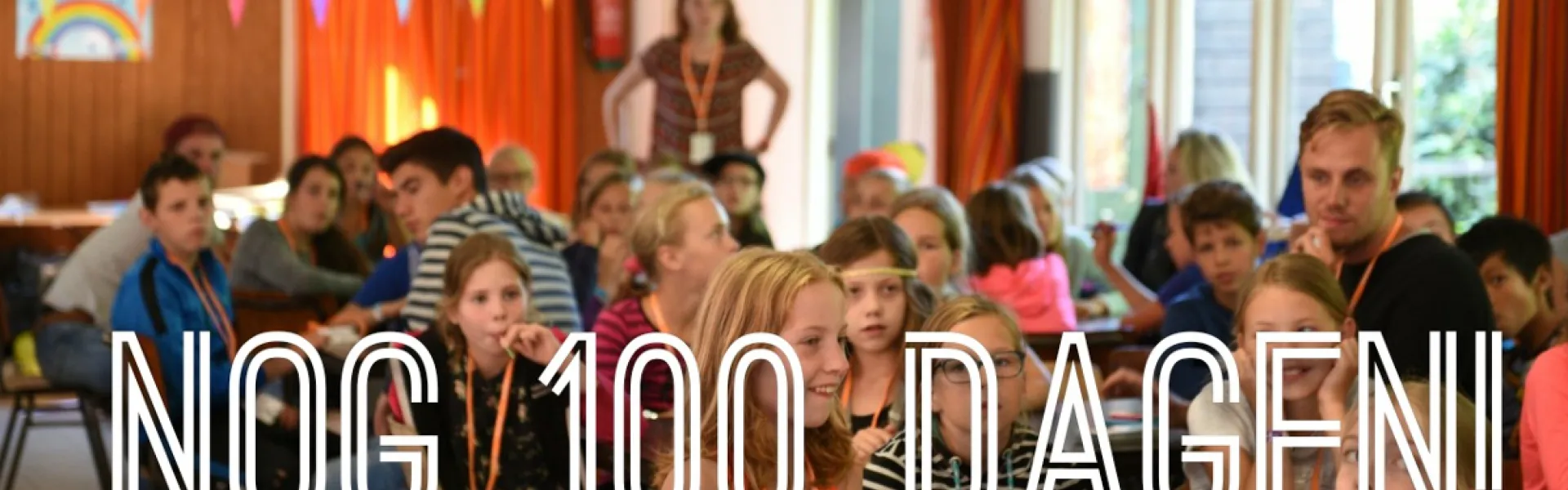 Deelnemers in een zaal met de tekst NOG 100 DAGEN eroverheen
