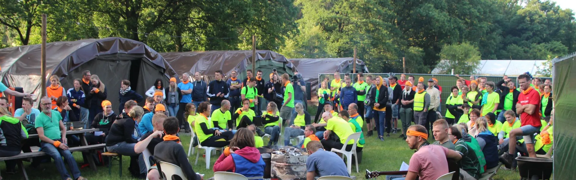 Deelnemers zitten op stoelen buiten voor de tent