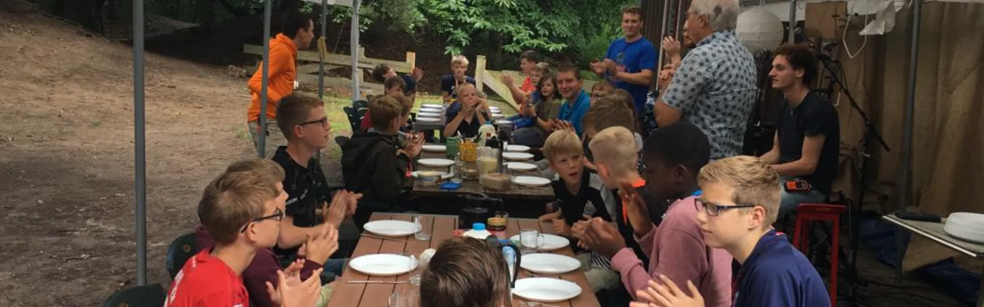 Deelnemers aan lange gedekte tafels onder een partytent