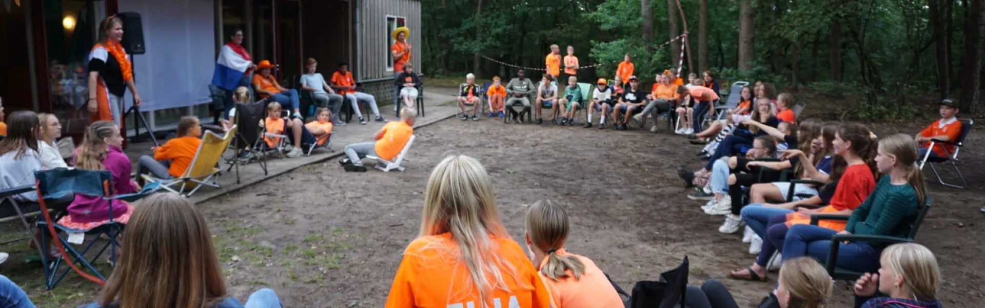 Deelnemers zitten in een kring op het terrein bij het kampgebouw