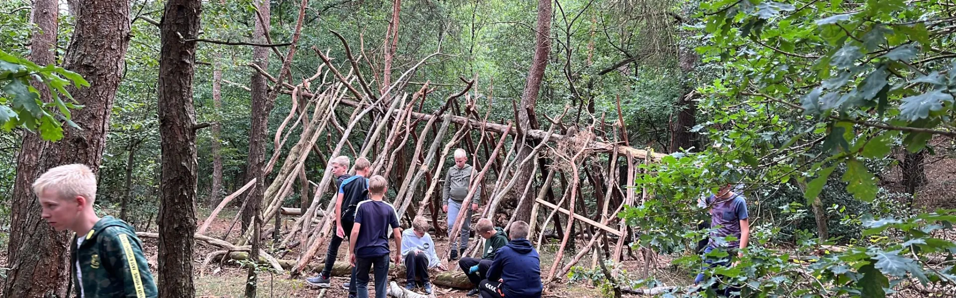 Deelnemers bouwen een hut van takken in het bos