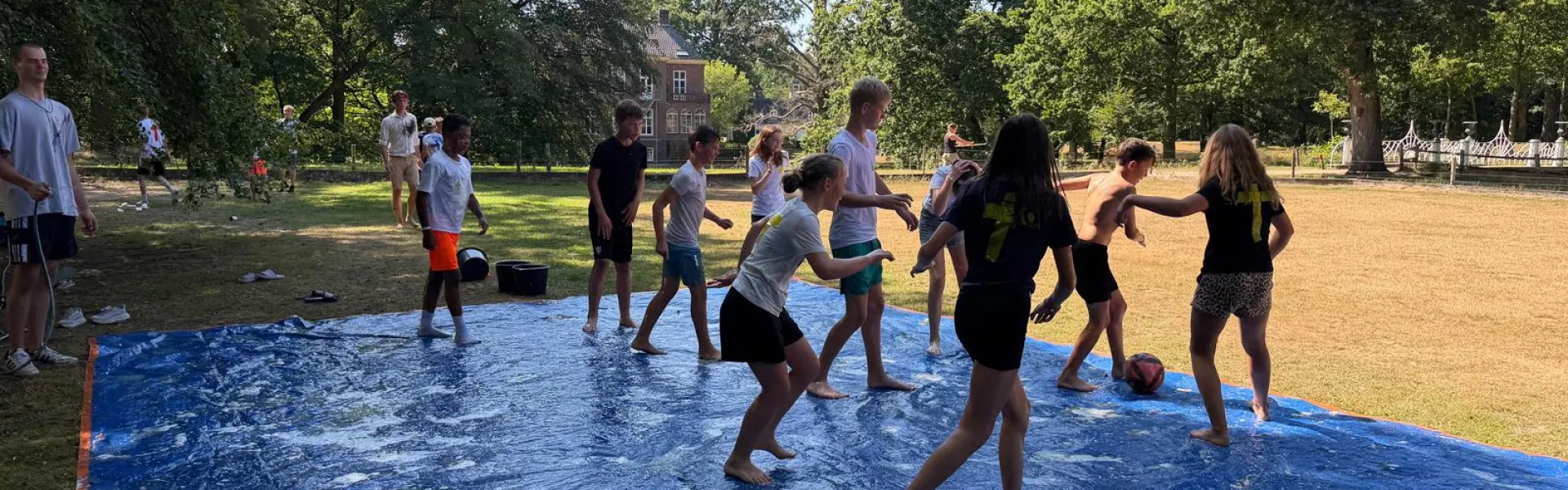 Deelnemers spelen op een nat zeil met glijbaan