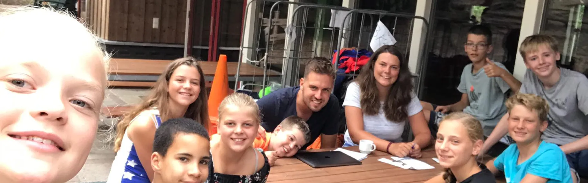 Deelnemers met feestmutsen aan tafel bij het kampgebouw