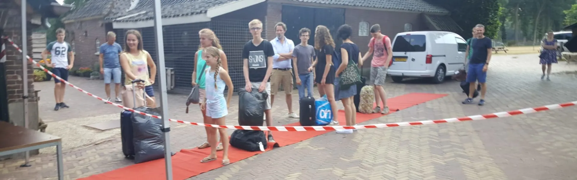 Deelnemers met bagage lopen over een rode loper