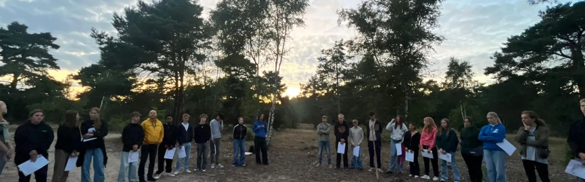 Deelnemers lopen in een rij over de zandvlakte bij zonsondergang