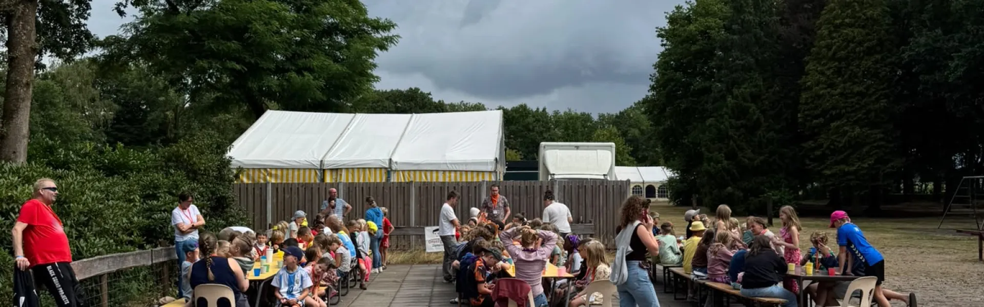 Deelnemers zitten op stoelen op het plein onder een bewolkte lucht