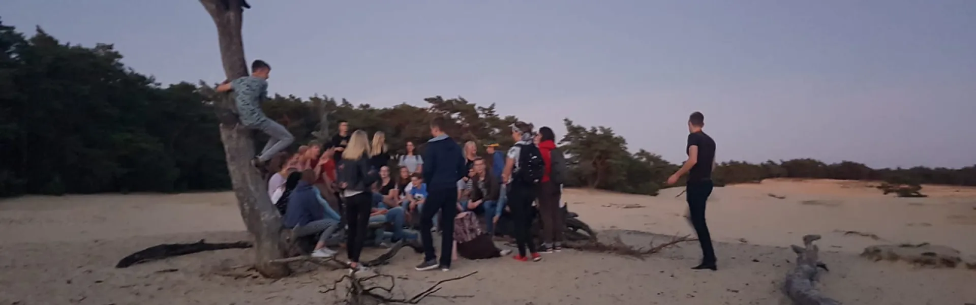 Deelnemers bij een kale boom op de zandvlakte in de avond