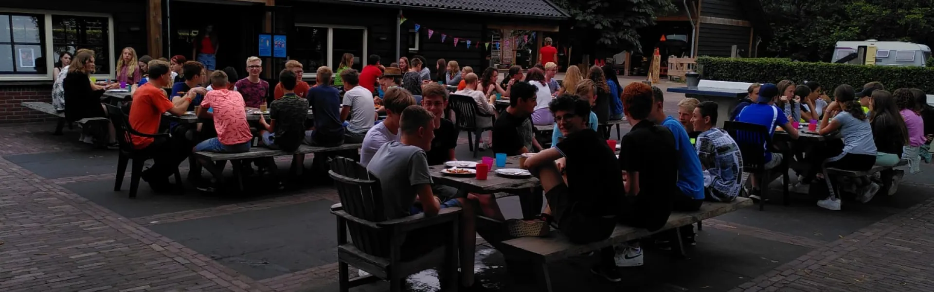 Deelnemers aan picknicktafels bij het kampgebouw