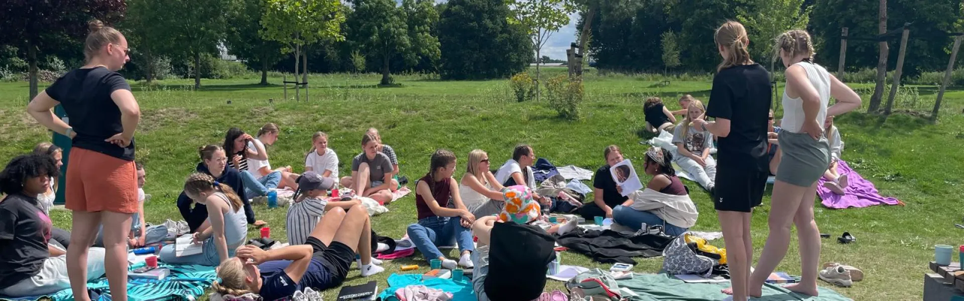 Deelnemers zitten op kleden in het gras